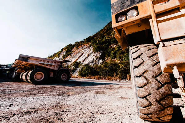 Close-up a large wheel of mining dump truck at an open pit near mountains area, lots of large mining dump truck parked in the backgrounds. Industrial, transportation concepts. Focus on wheel.