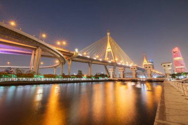 Alacakaranlıkta bir otoyol kavşağı ve asma köprü manzarası, Tayland 'daki Chao Phraya Nehri' nin yüzeyinde yansıyan ışıklar..