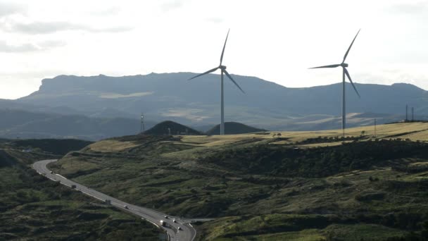 Windenergieanlagen bewegen sich am Berg zusammen eine Straße bei bewölktem Himmel — Stockvideo