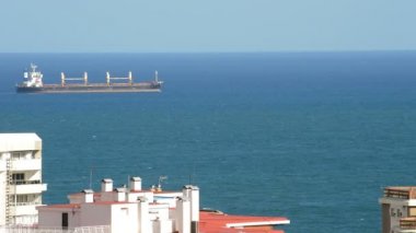 Ticaret gemisi ön planda şehir binaları ile yelken