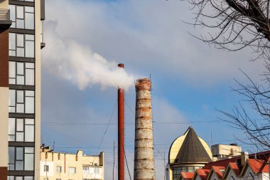 Şehrin arka planında, termal kazan dairesinin bacasından çıkan beyaz duman. Ekoloji sorunları. Isıtma sezonu.