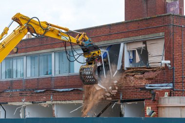 Demolition of an old building with a long reach machine hydraulic jaw. Regeneration of a space for new, modern building. clipart