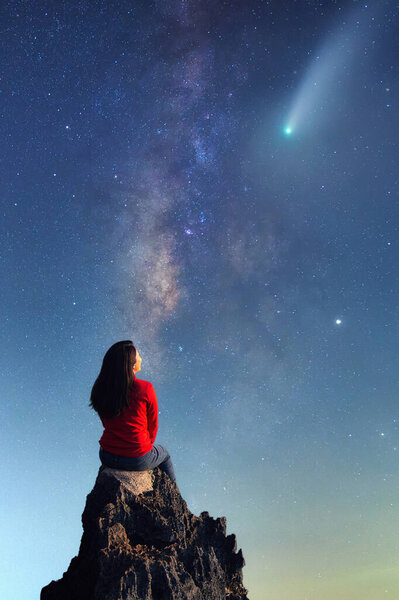 A young woman watching the beauty of the Milky Way and a meteor on the rocks.