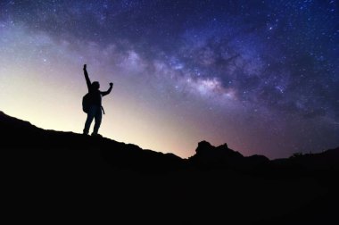 Samanyolu 'yla manzara. Gece gökyüzü yıldızlarla ve dağda duran mutlu bir adamın silüetiyle, Başarı ya da kazanan, lider konsepti. Gürültülü yüksek izo.