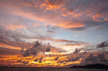 Bir adanın siyah siluetiyle deniz ufkunun üzerinde güzel bir tropikal gün batımı. Seyşeller
