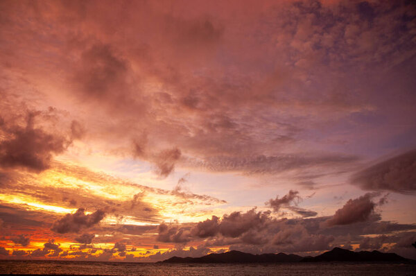 Beautiful tropical sunset over the sea horizon with black silhouette of an island. Seychelles