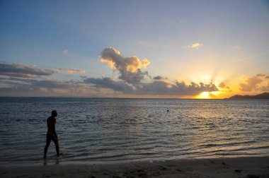 Gün batımında sahilde kolları olan bir adamın silueti.