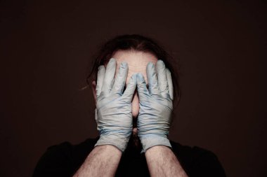 Covid-19 / Coronavirus. Bir hastalığın insan portresi. Kafası elinde koruyucu mavi lateks eldiven giyen bir adam.