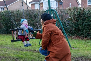 Anne oğlunu salıncakta sallıyor. Anne ve çocuğu dışarıda eğleniyorlar. Mutlu aile kavramı
