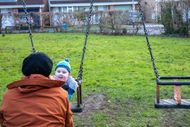 Anne oğlunu salıncakta sallıyor. Anne ve çocuğu dışarıda eğleniyorlar. Mutlu aile kavramı