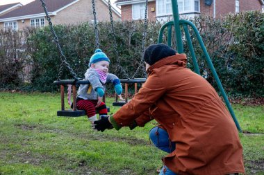 Anne oğlunu salıncakta sallıyor. Anne ve çocuğu dışarıda eğleniyorlar. Mutlu aile kavramı