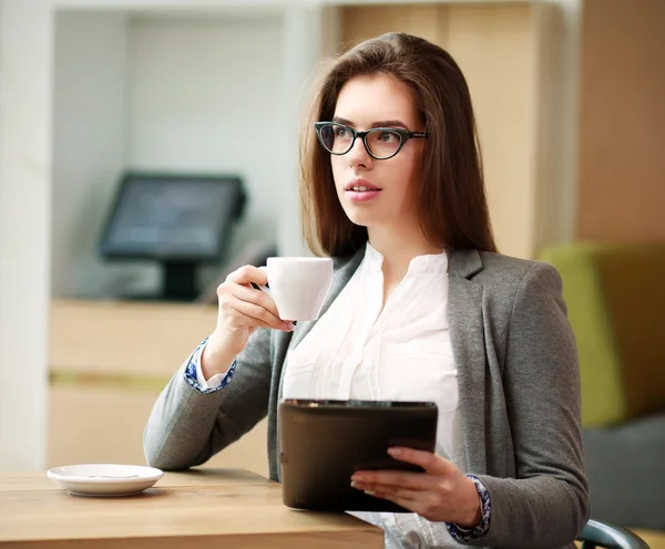 Jonge zakenvrouw met een kopje koffie werkzaam in kantoor — Stockfoto