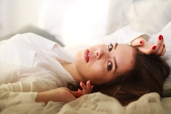 Hermosa chica pensativa acostada en la cama sobre el fondo de la luz del sol —  Fotos de Stock