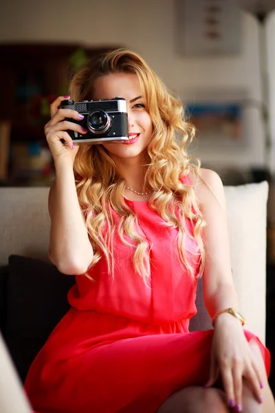 Smiling woman in dress with retro camera, on couch at home — Stock Photo, Image