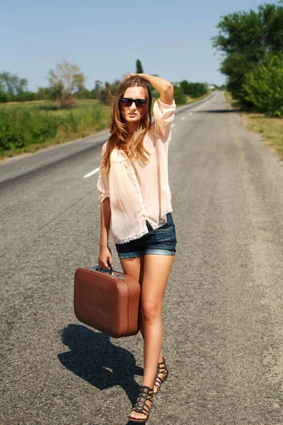 Jeune femme avec valise auto-stop sur la route à la campagne — Photo