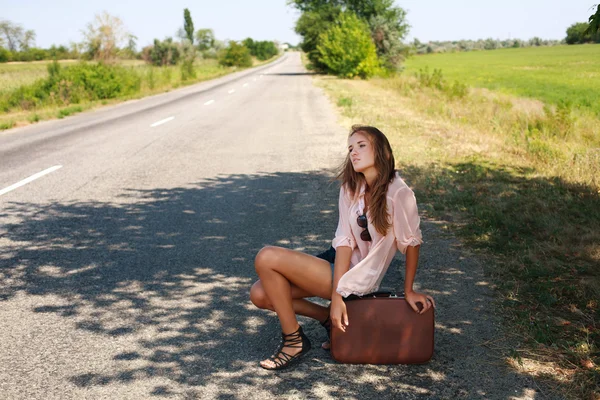 Mujer cansada con maleta haciendo autostop en la carretera en el país —  Fotos de Stock