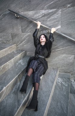 Taş bir duvarın arkasında, modaya uygun siyah elbiseli bir kız, modern şehir mimarisi, moda tarzı fotoğraf.