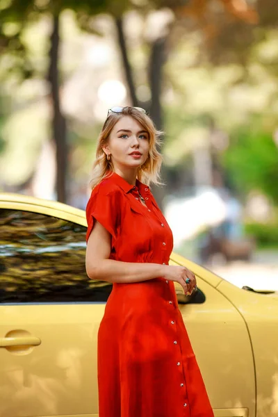 都会の公園で黄色の車の近くの赤いドレスを着た若い魅力的で夢のようなビジネス女性 — ストック写真