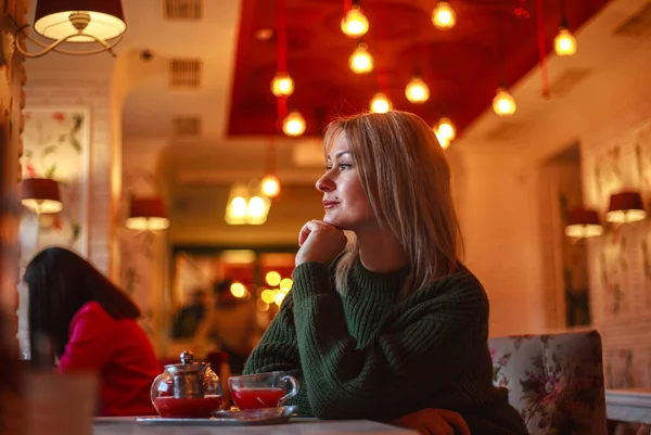 Woman in sweater sitting in a restaurant with a cup of fruit tea and looking out the window