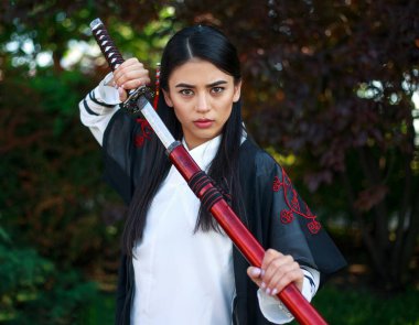 Geleneksel kimano giymiş genç Asyalı bir kız çiçek açan bir bahçede Japon bir kılıç katana ile savaşçı bir kadın suretinde.