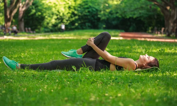 草の上の緑の公園で体を伸ばしフィットネス演習を行う若い女性 自然の中で健康的なライフスタイル — ストック写真