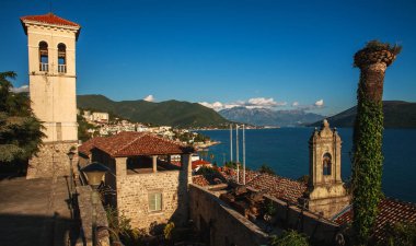 Deniz kıyısındaki tatil köyünün güzel manzarası, körfezdeki yeşil dağlar ve açık mavi gökyüzü, Karadağ, Herceg Novi