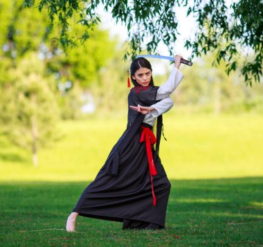 Young asian woman in traditional kimono trains fighting techniques with katana sword, samurai warrior girl