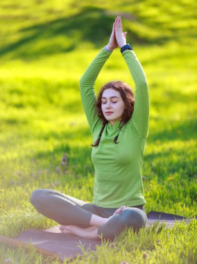 Çimlerin üzerindeki yeşil parktaki kız yoga meditasyonu yapıyor. Açık havada sağlıklı bir yaşam sürüyor.