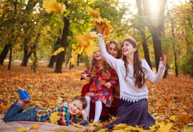 Üç çocuklu bir aile, sonbahar parkında mevsimlik tatil haftasonu tatillerinde düşmüş sarı yapraklarla eğleniyor.