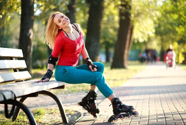 Hermosa joven en patines sentada en el banco del parque — Foto de Stock