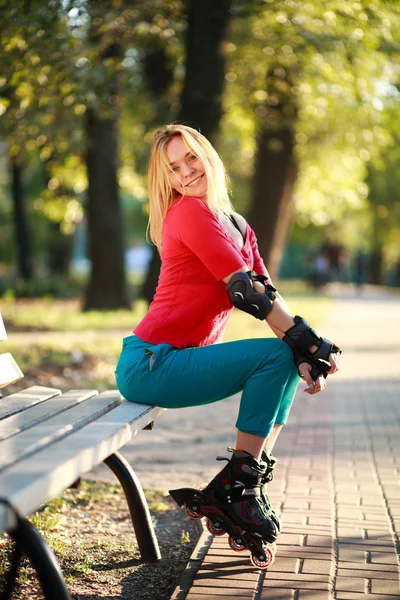 Vacker ung kvinna i rullskridskor sitter på parkbänk — Stockfoto