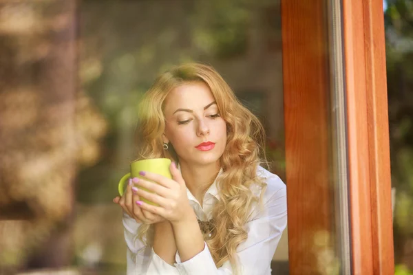 Eftertänksam kvinna dricker kaffe hemma, tittar ut genom fönstret — Stockfoto