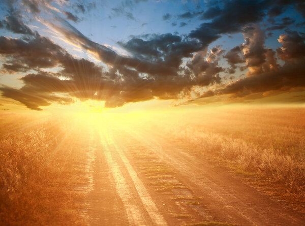 Bright colorful sunset over country road on the background of a dramatic sky