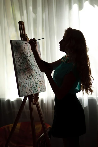 Backlight portrait,  silhouette woman artist draws paint picture on easel — Stock fotografie