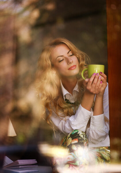 Dreamy woman with a cup of coffee in cafe, enjoying the aroma