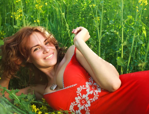 Sonriente mujer joven sexy acostada en la hierba en un vestido rojo —  Fotos de Stock