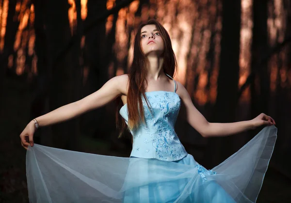 Giovane ragazza in un lungo vestito blu ballare nella foresta scura — Foto Stock