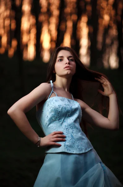 Молодая девушка в длинном голубом платье позирует в темном лесу — стоковое фото