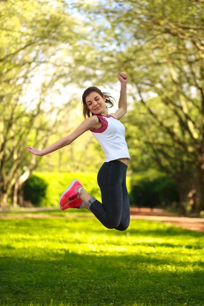 緑の夏の公園でジャンプ幸せな陽気な女の子 — ストック写真