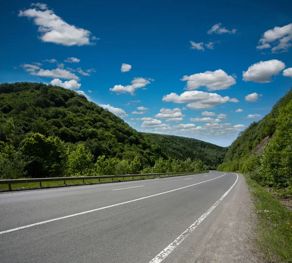 Empty asphalt road highway in the forested mountains, sky