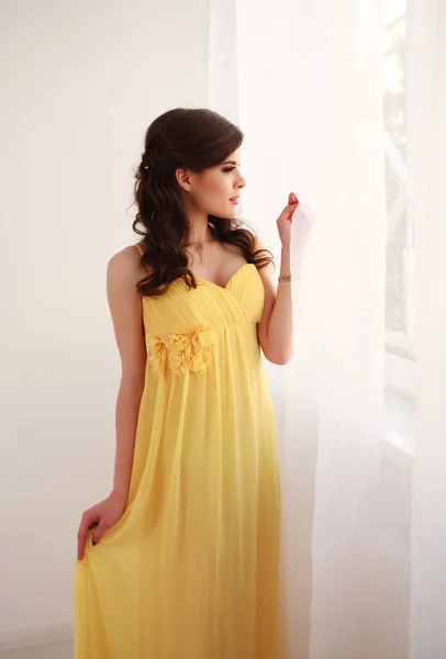 Moda mujer joven en vestido largo amarillo, mirando por la ventana —  Fotos de Stock