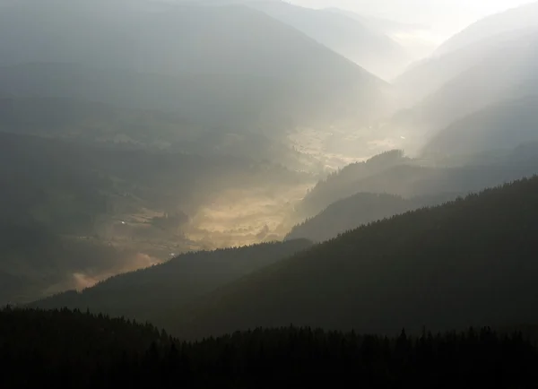 Mountain valley village in the fog and sun rays of dawn — Stock Photo, Image