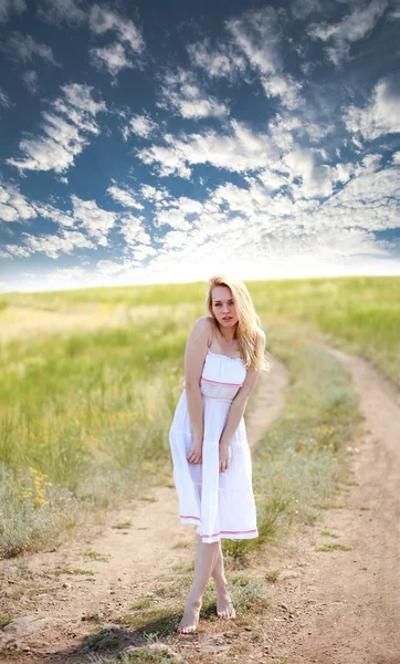 Чувственная девушка в платье на проселочной дороге на драматическом небе — стоковое фото