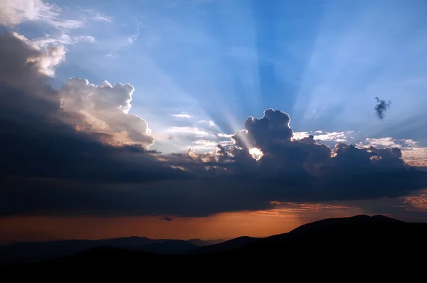 Dağın üstünden mavi gökyüzü üzerinde Bulutların arasından güneş ışınları şafak — Stok fotoğraf