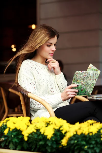 Meisje zit aan een tafel in een zomerterras en het lezen van een kaart — Stockfoto