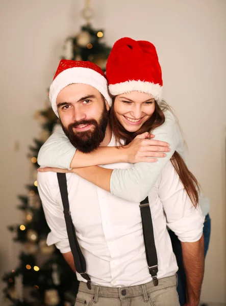 Glada par i röda hattar på bakgrunden av julgran — Stockfoto