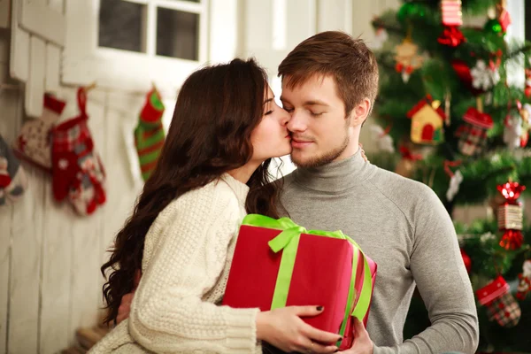 Счастливая пара с подарком дома на фоне Рождества — стоковое фото