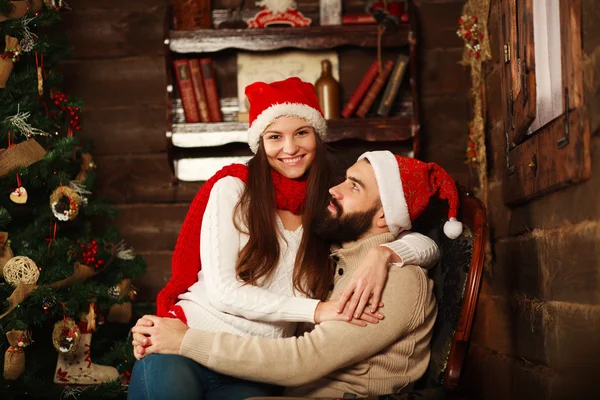 Casal alegre em chapéus de Natal se divertindo em uma casa de campo — Fotografia de Stock