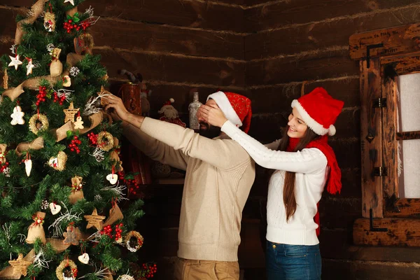 Alegre pareja decora un árbol de Navidad en una casa de campo — Foto de Stock