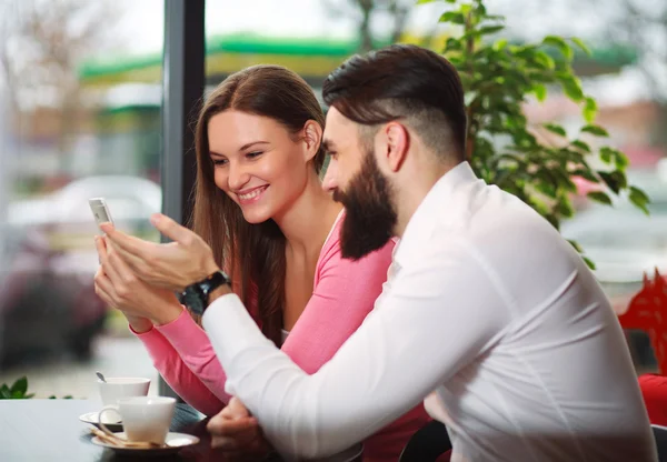 Feliz jovem casal no café olhando para um smartphone — Fotografia de Stock